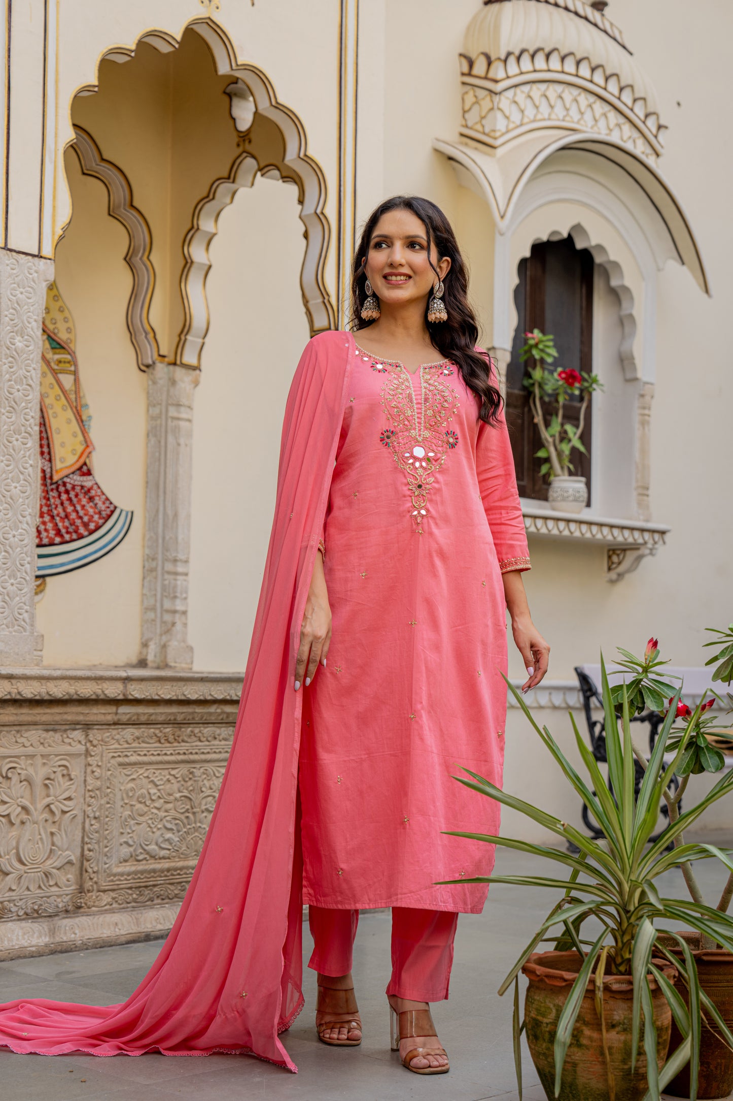 Woman in a pink traditional Kurta set for wedding standing in front of an ornate building.