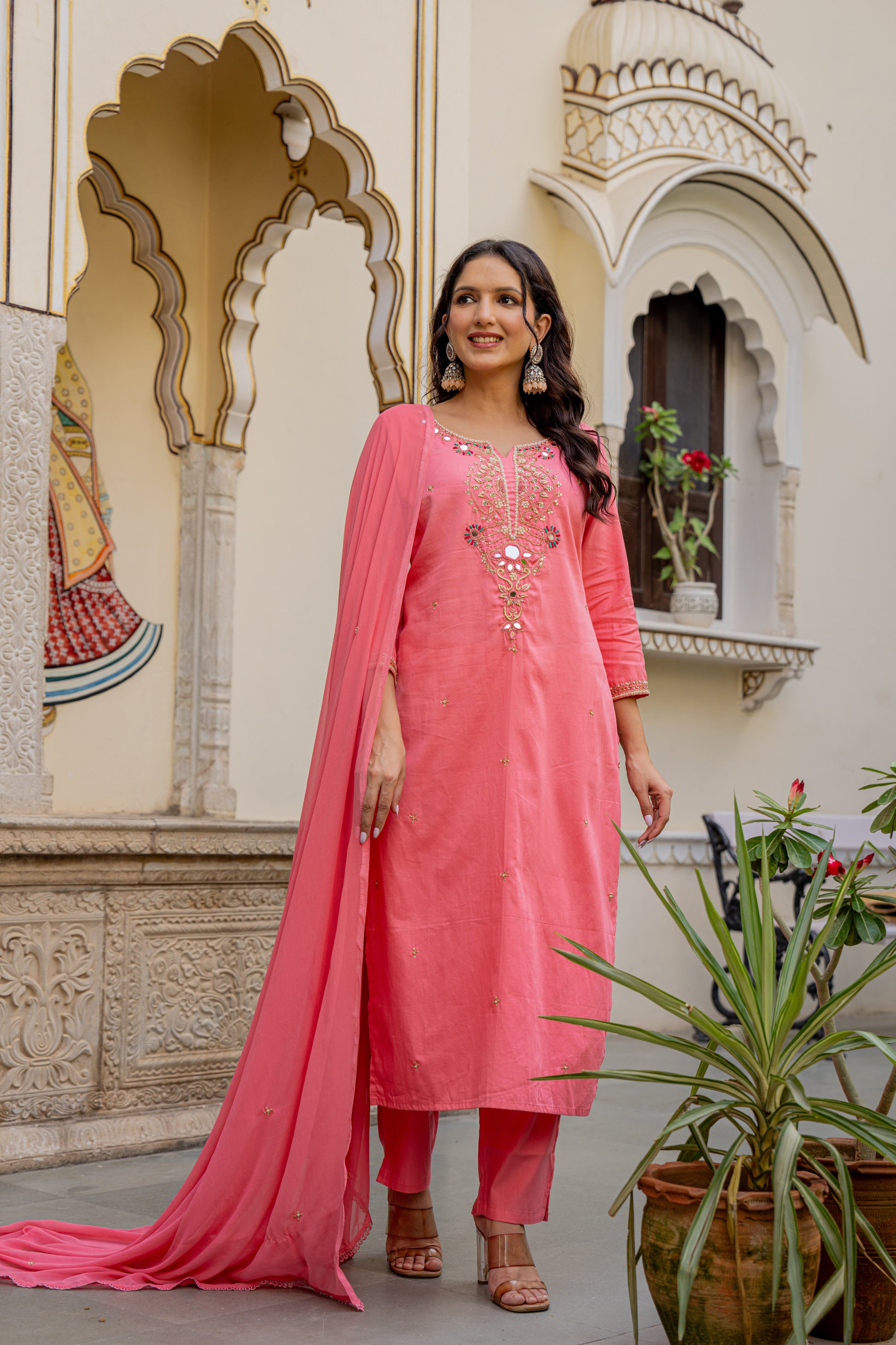 Woman in a pink traditional Kurta set for wedding standing in front of an ornate building.