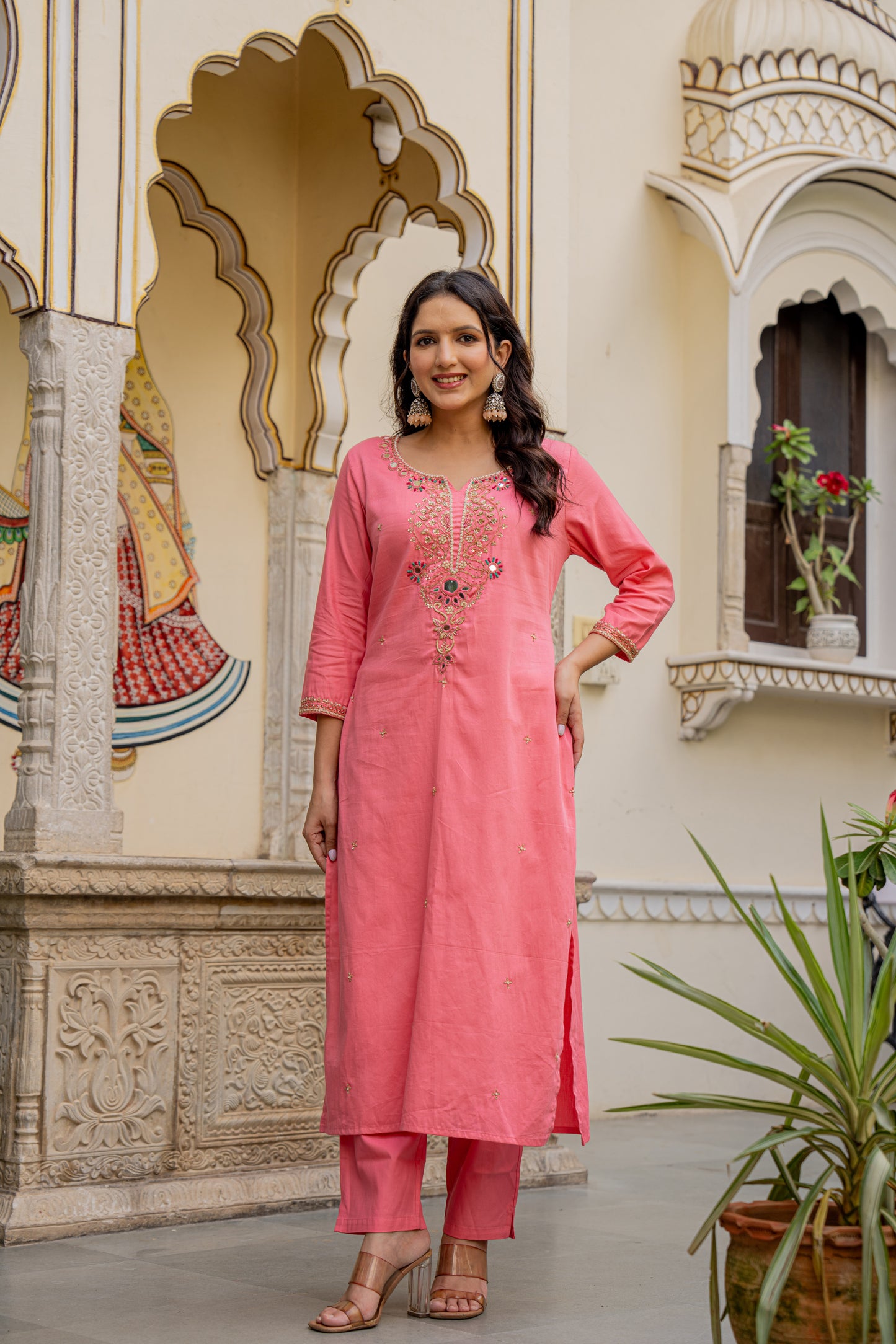 Woman in a pink traditional outfit standing in front of ornate architecture.