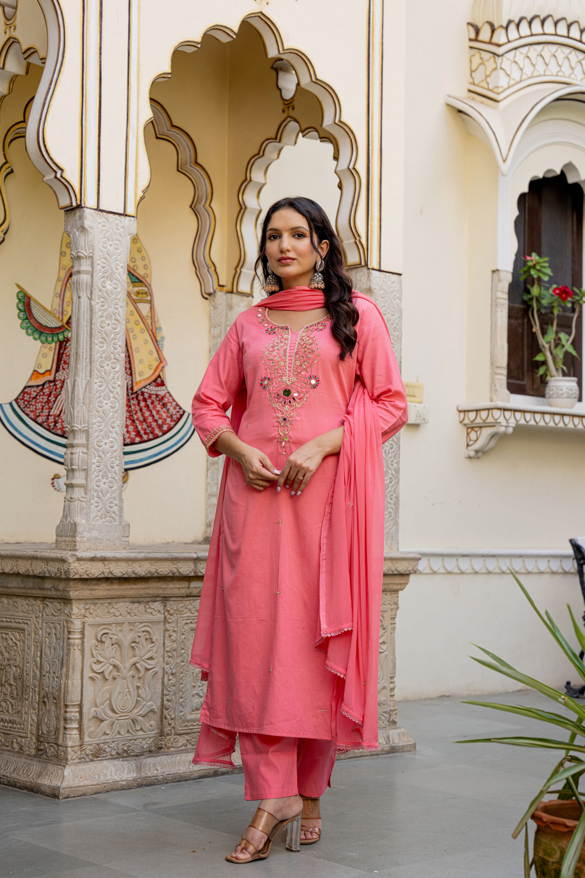 Woman in a pink traditional outfit standing in an ornate indoor setting.