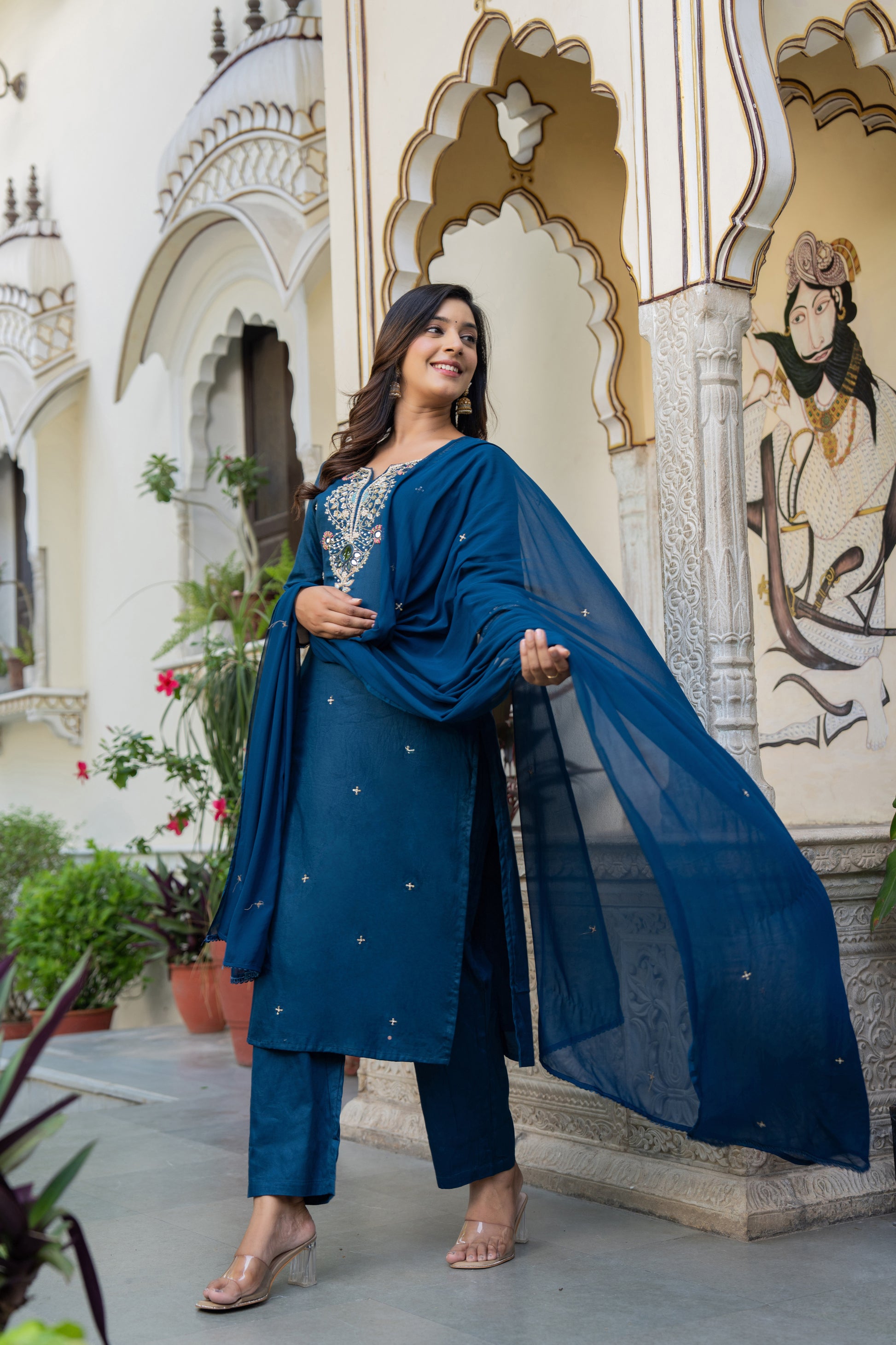Woman in a blue wedding kurta set standing in front of an ornate building.