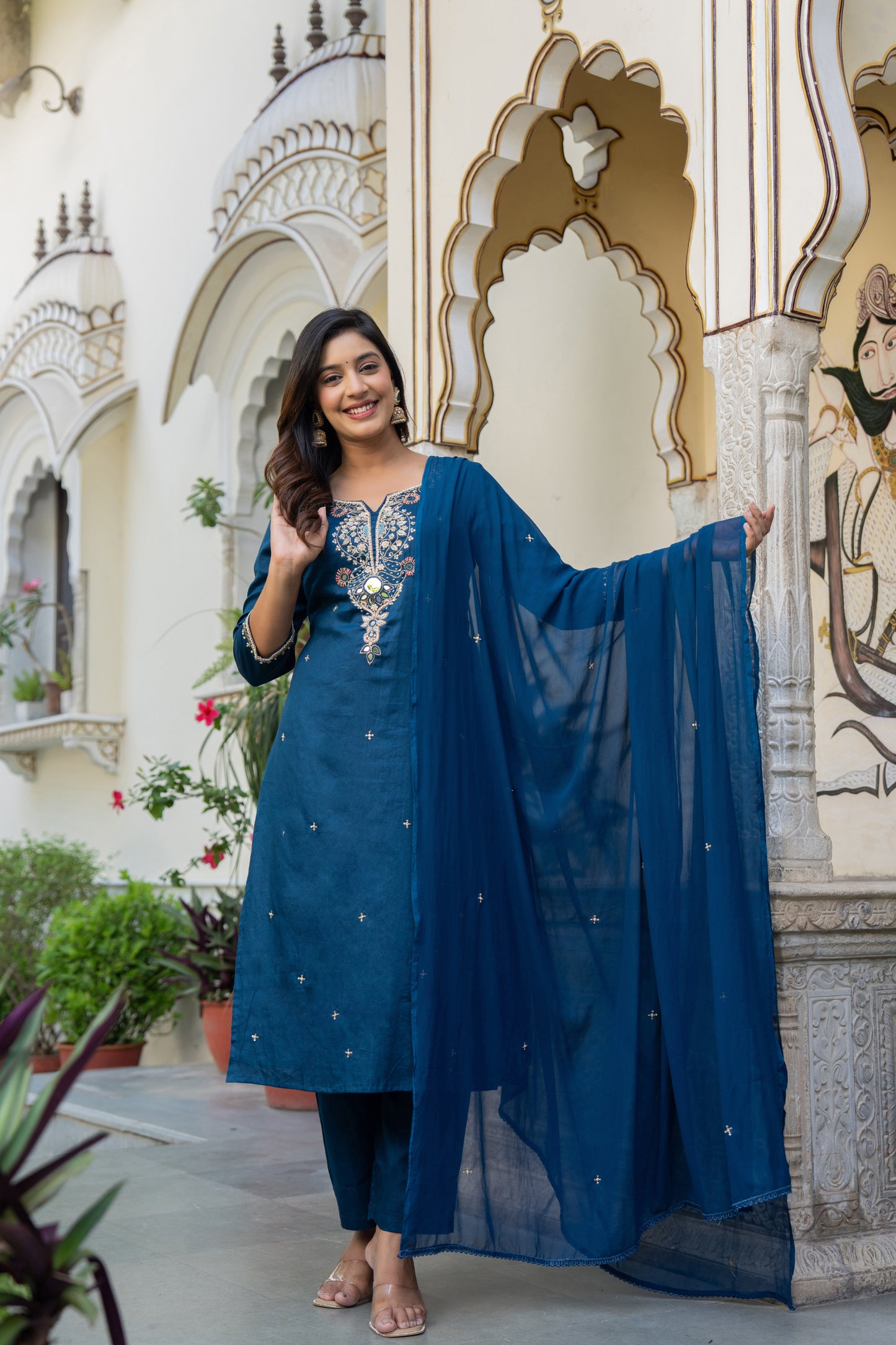 Woman in a blue traditional outfit  which is a wedding kurta set for women standing in front of decorative walls.