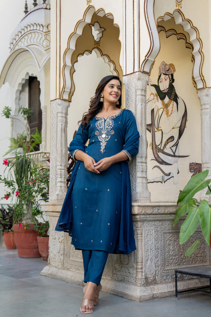 Woman in a Teal blue Kurta set made for wedding wear standing in front of ornate architectural wall.