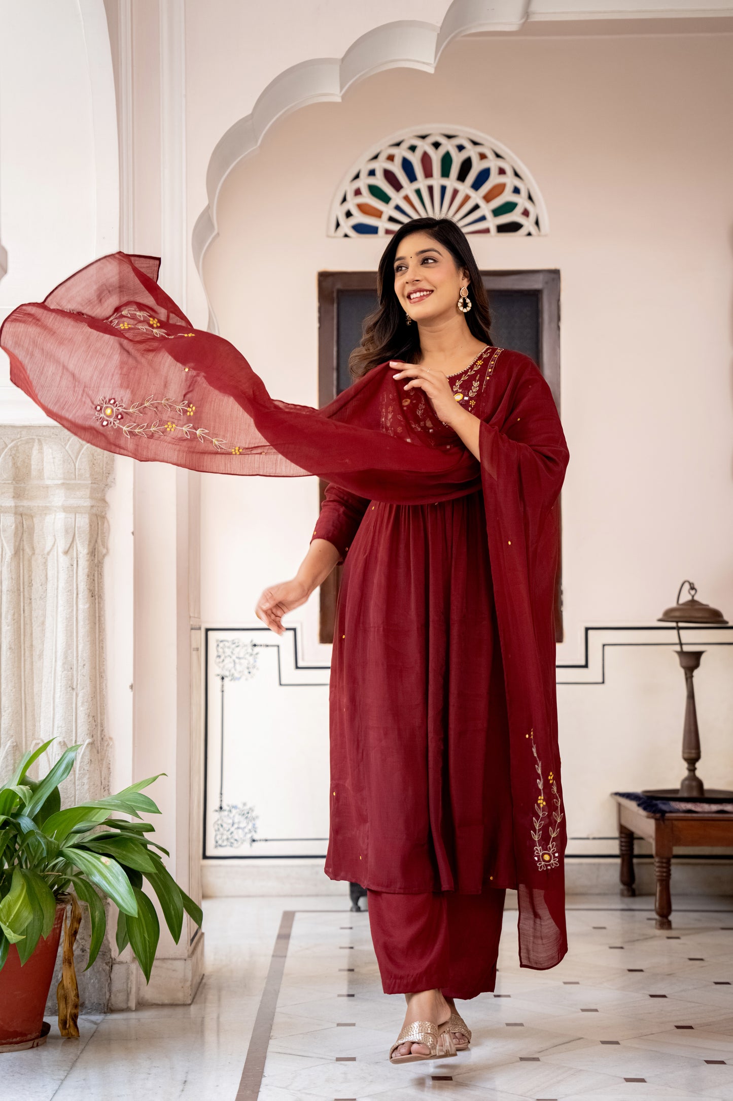 Woman in a red traditional outfit standing in an ornate room with decorative arches.