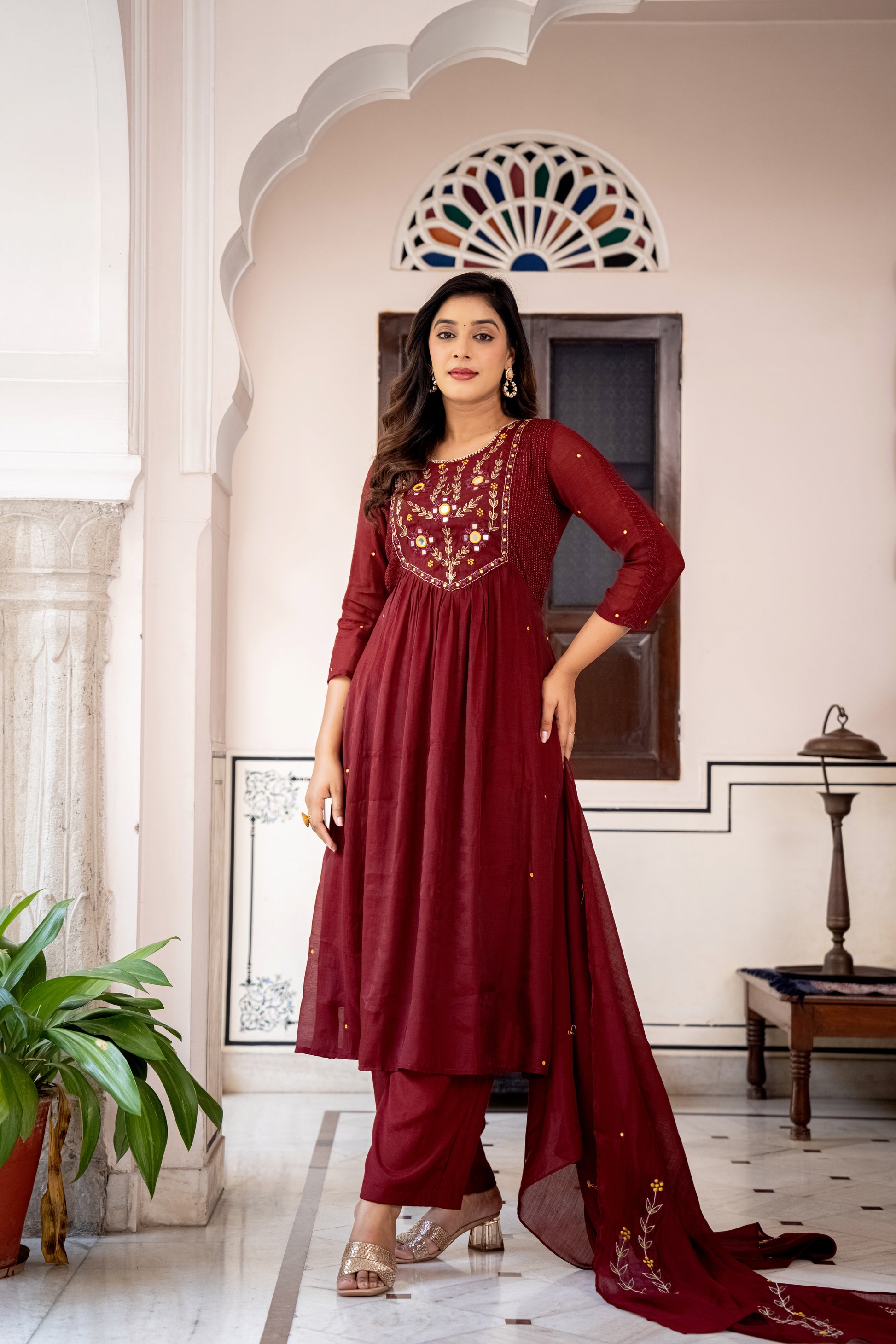 Woman in a red wedding kurta set standing in an elegant interior setting.