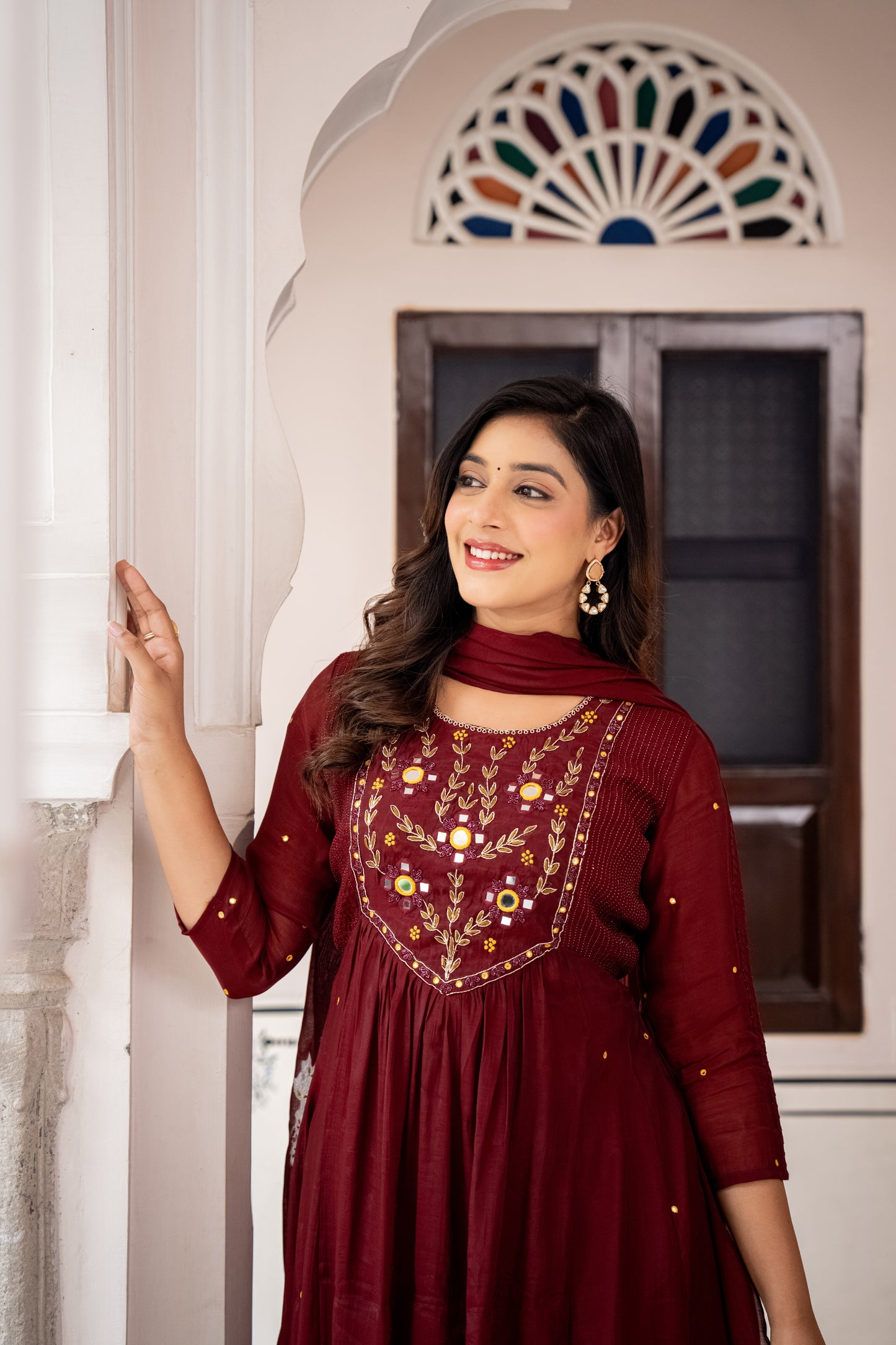 Woman wearing a red embroidered dress standing indoors.