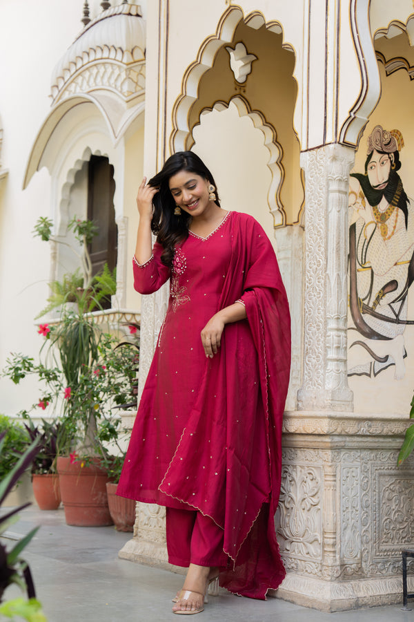 Woman in a red traditional outfit which is a kurta set designed for wedding standing in front of decorative architecture.
