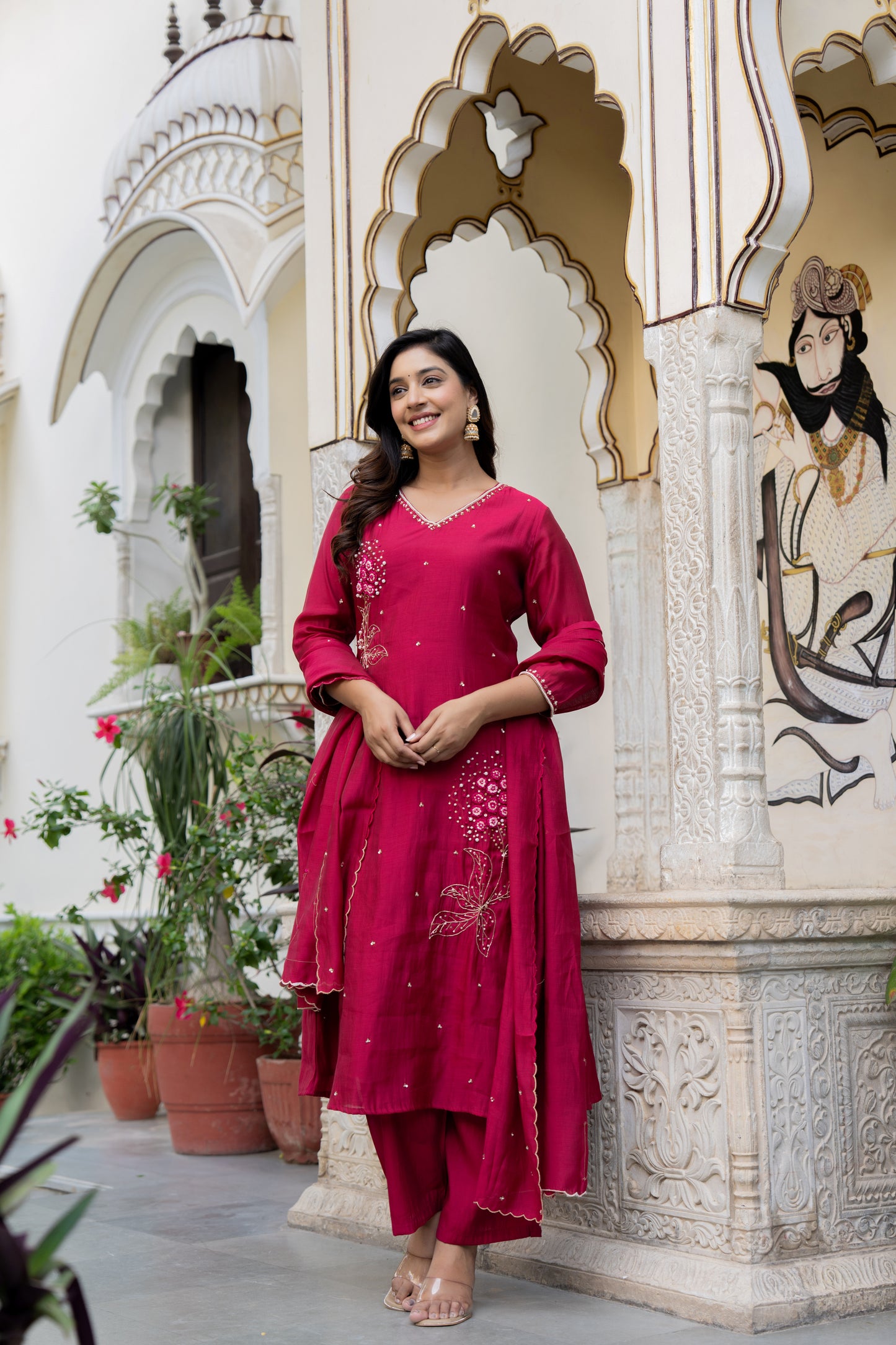 Woman in a Pink kurta set standing in front of an ornate architectural background