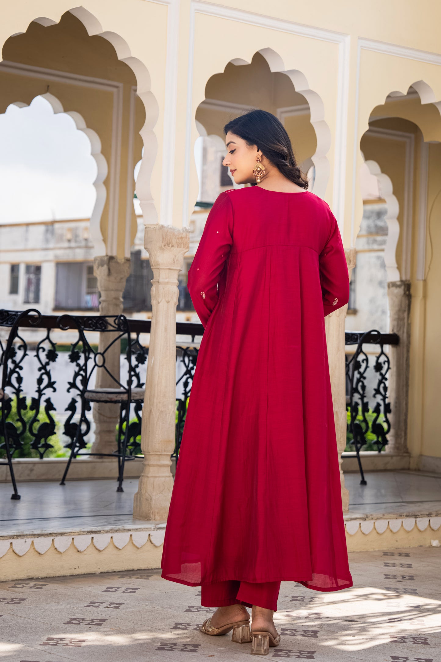 Woman in a red dress standing on a balcony with decorative arches and railings.