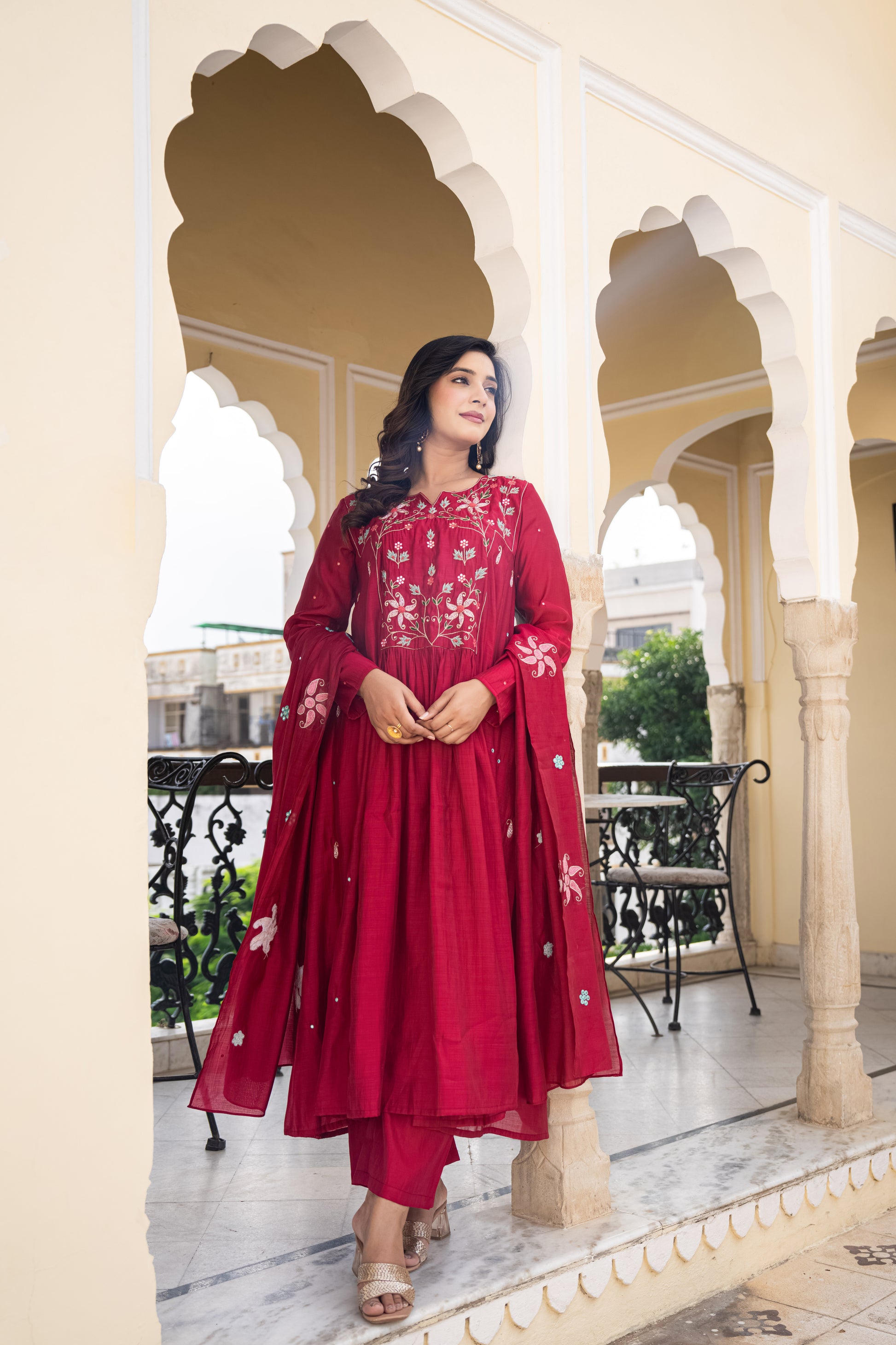 Woman in a red traditional outfit standing in an ornate architectural setting.