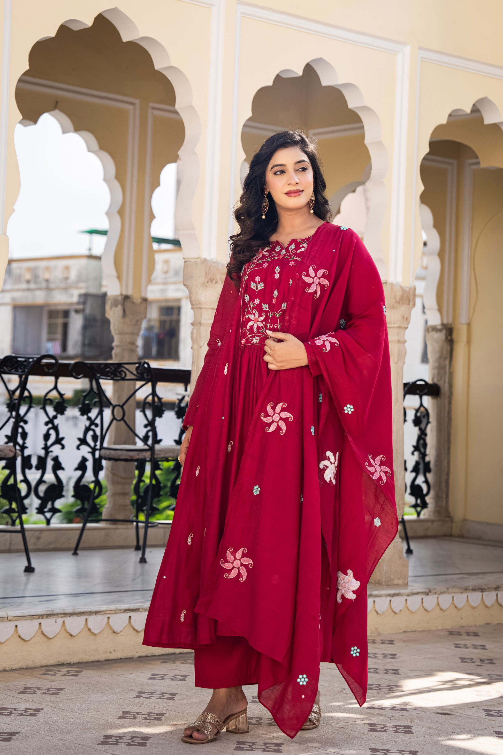 Woman in a red wedding wear kurta set standing in an ornate architectural setting.