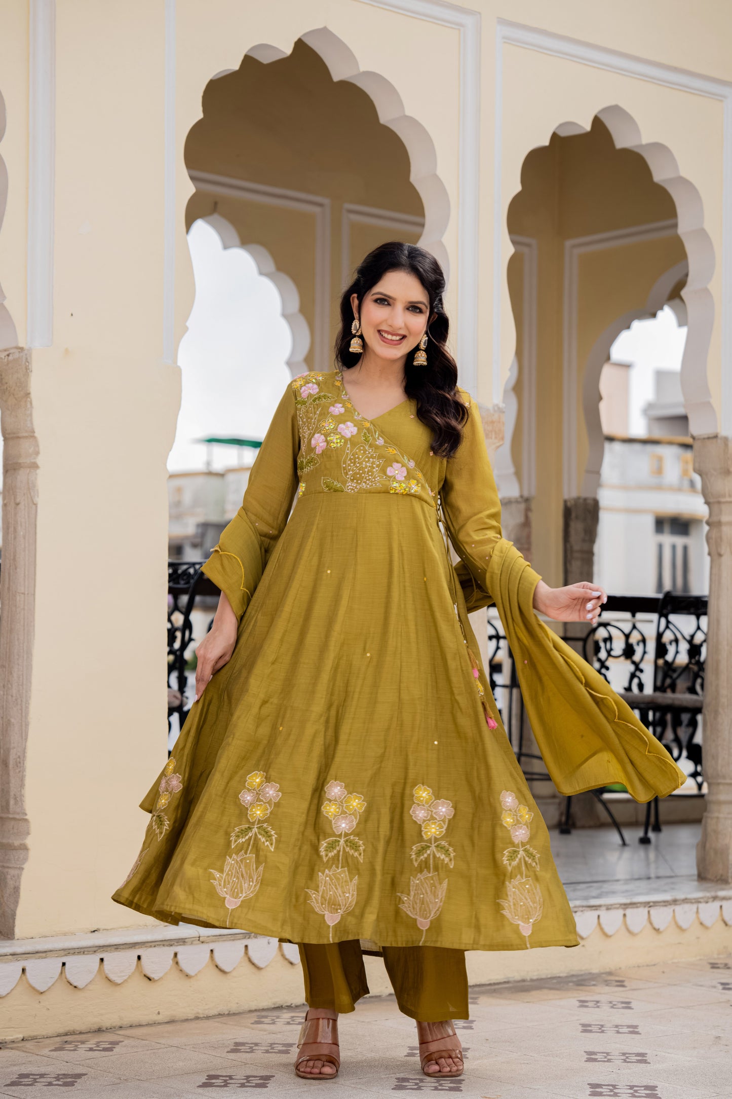 Green anarkali kurta set worn by a woman in front of decorative arches, representing graceful ethnic sets for women