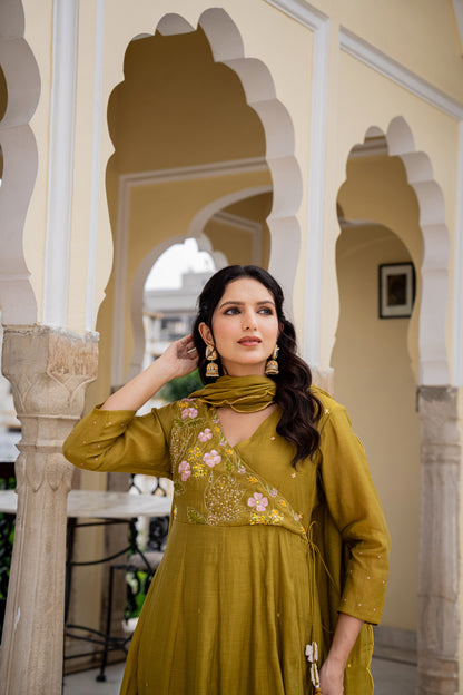 Woman in a mustard yellow traditional outfit with floral details standing in front of architectural arches.