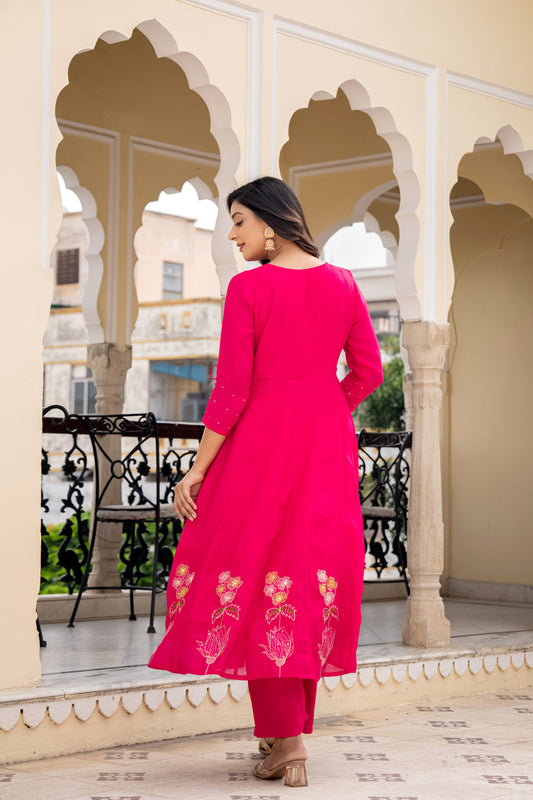 Woman in a bright pink traditional outfit standing on a balcony with decorative arches.
