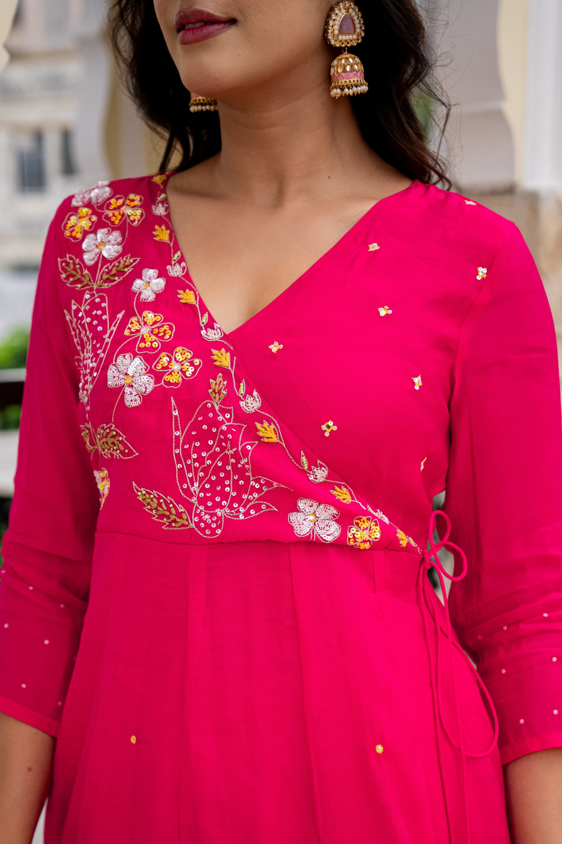 Woman wearing a bright pink traditional outfit with floral and paisley patterns.