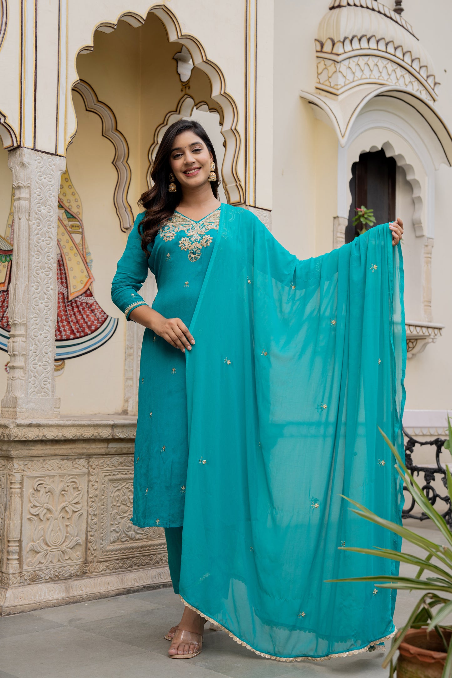 Woman in a teal green traditional outfit standing before an ornate building, highlighting a stunning wedding kurta set for women.