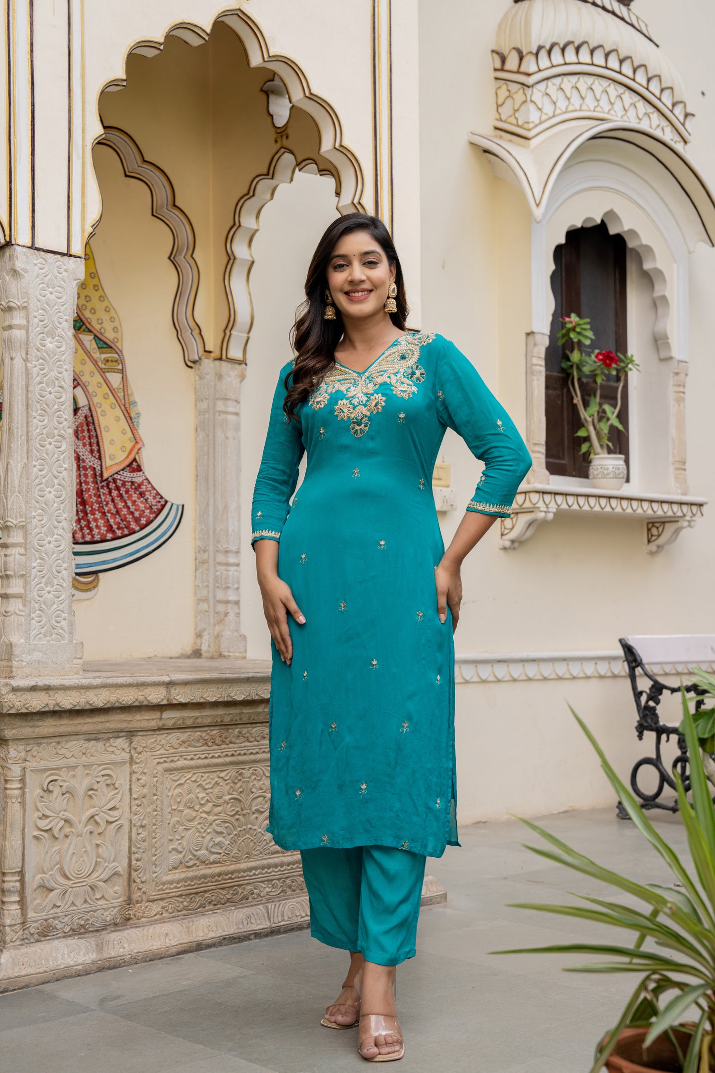 Woman in a teal traditional outfit standing in front of ornate architecture.