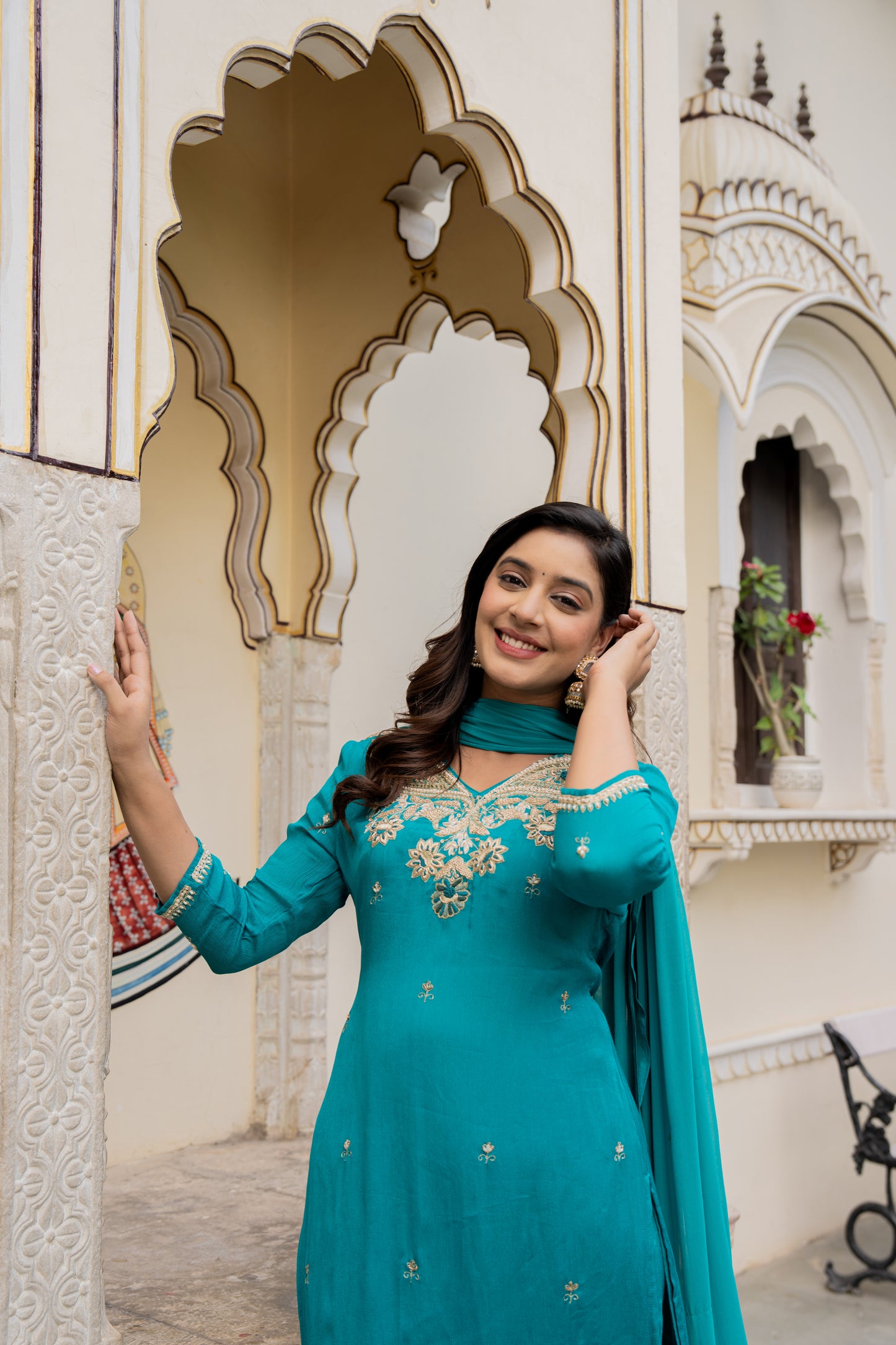 Teal green traditional wedding kurta set for women worn by a lady, captured in front of an ornate building.