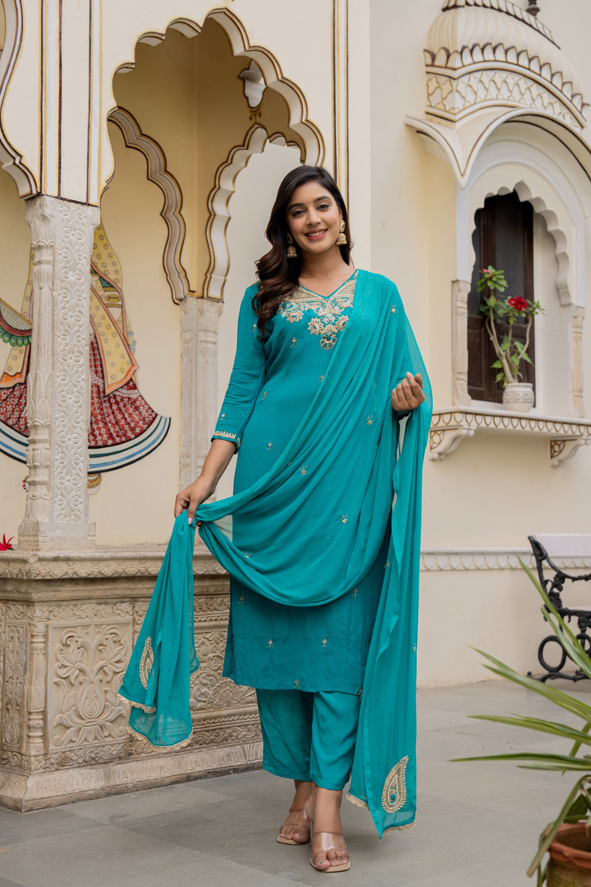 Woman in a teal traditional outfit standing in front of decorative architecture.