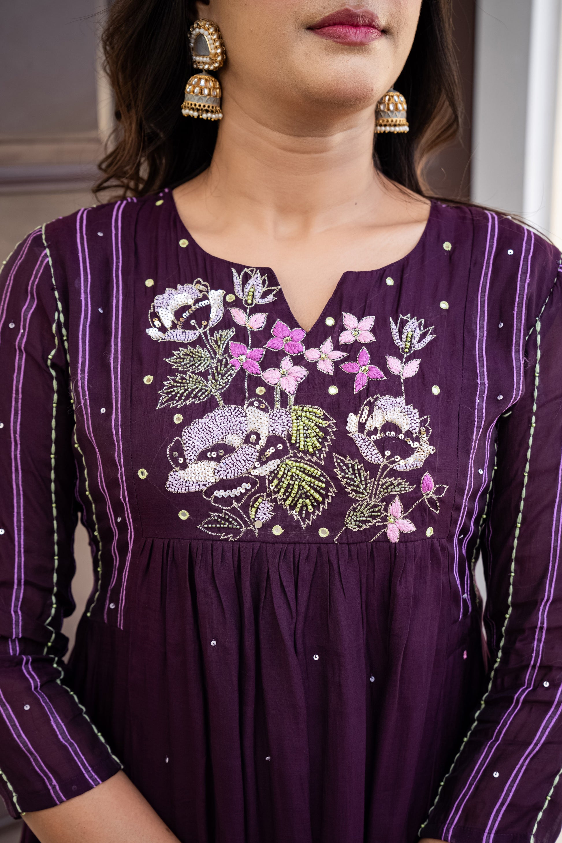 Purple embroidered dress with floral patterns and a face design, worn by a person.