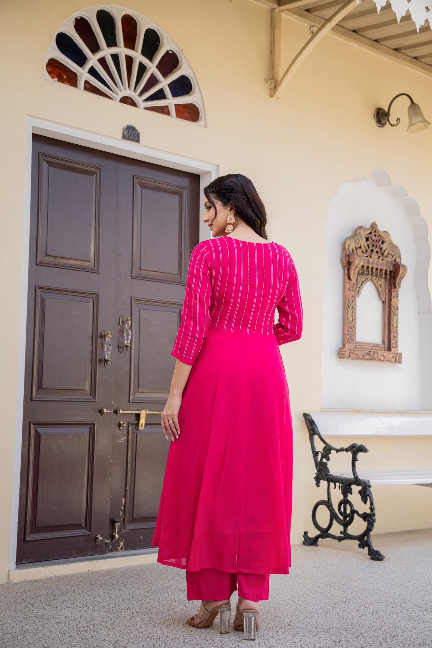 Woman in a bright pink traditional outfit standing in front of a decorative door.
