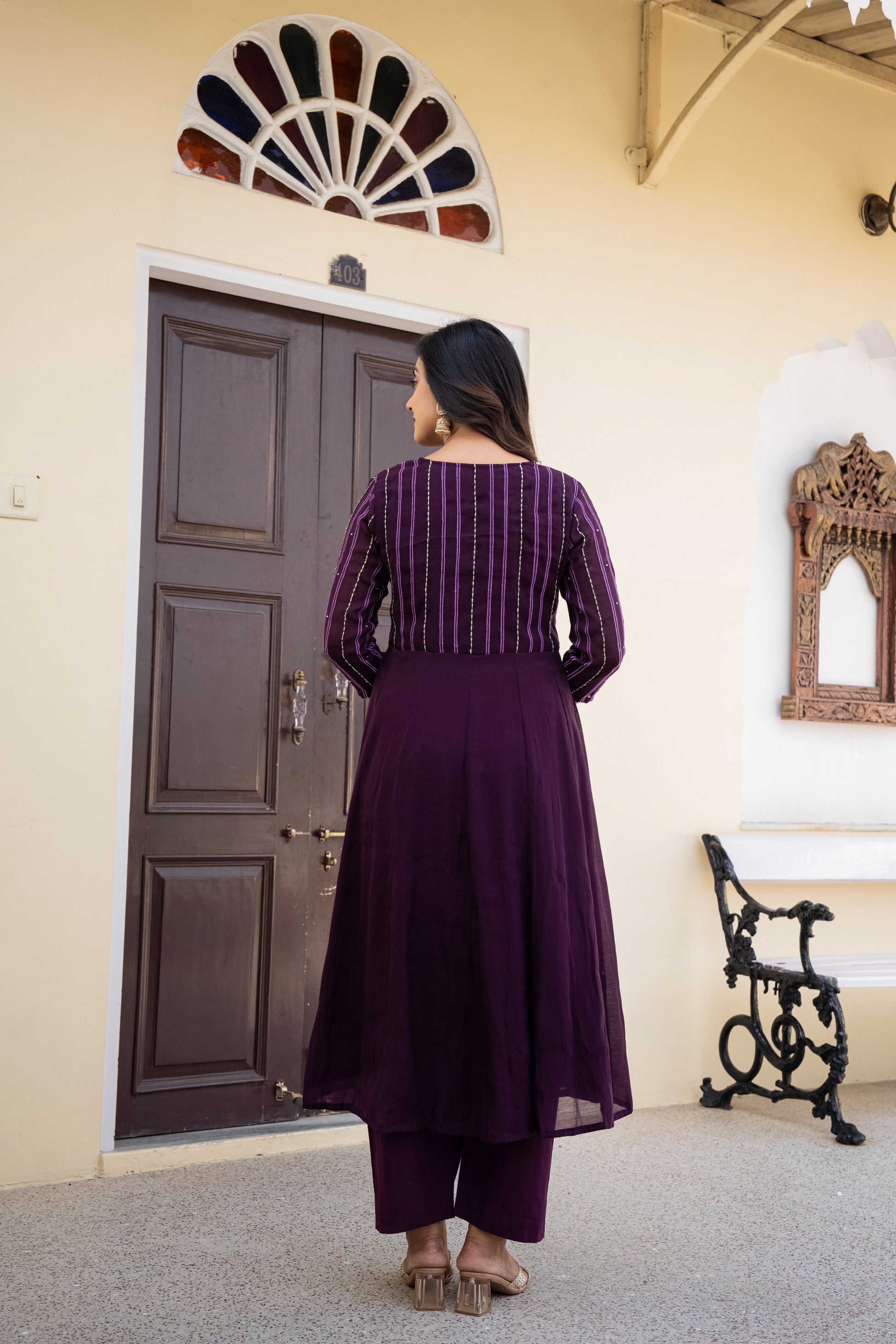 Woman in a purple outfit standing in a room with a door and bench.