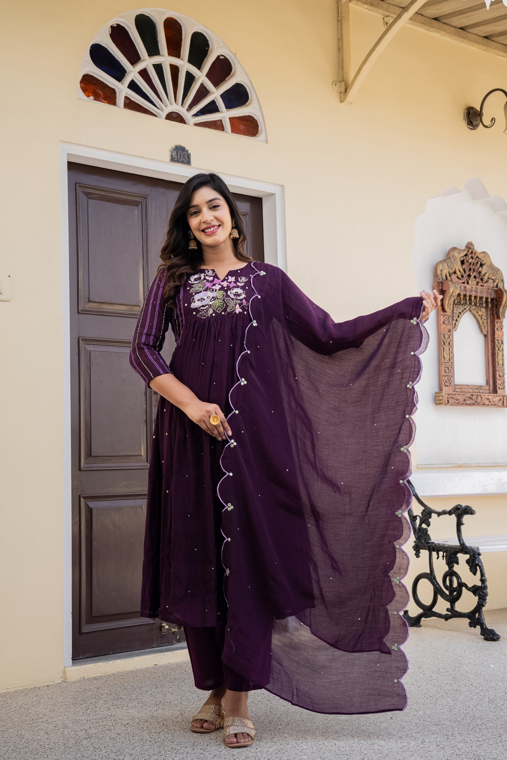 Woman wearing a purple anarkali kurta set with dupatta standing in a room filled with decor, reflecting classic ethnic sets for women.