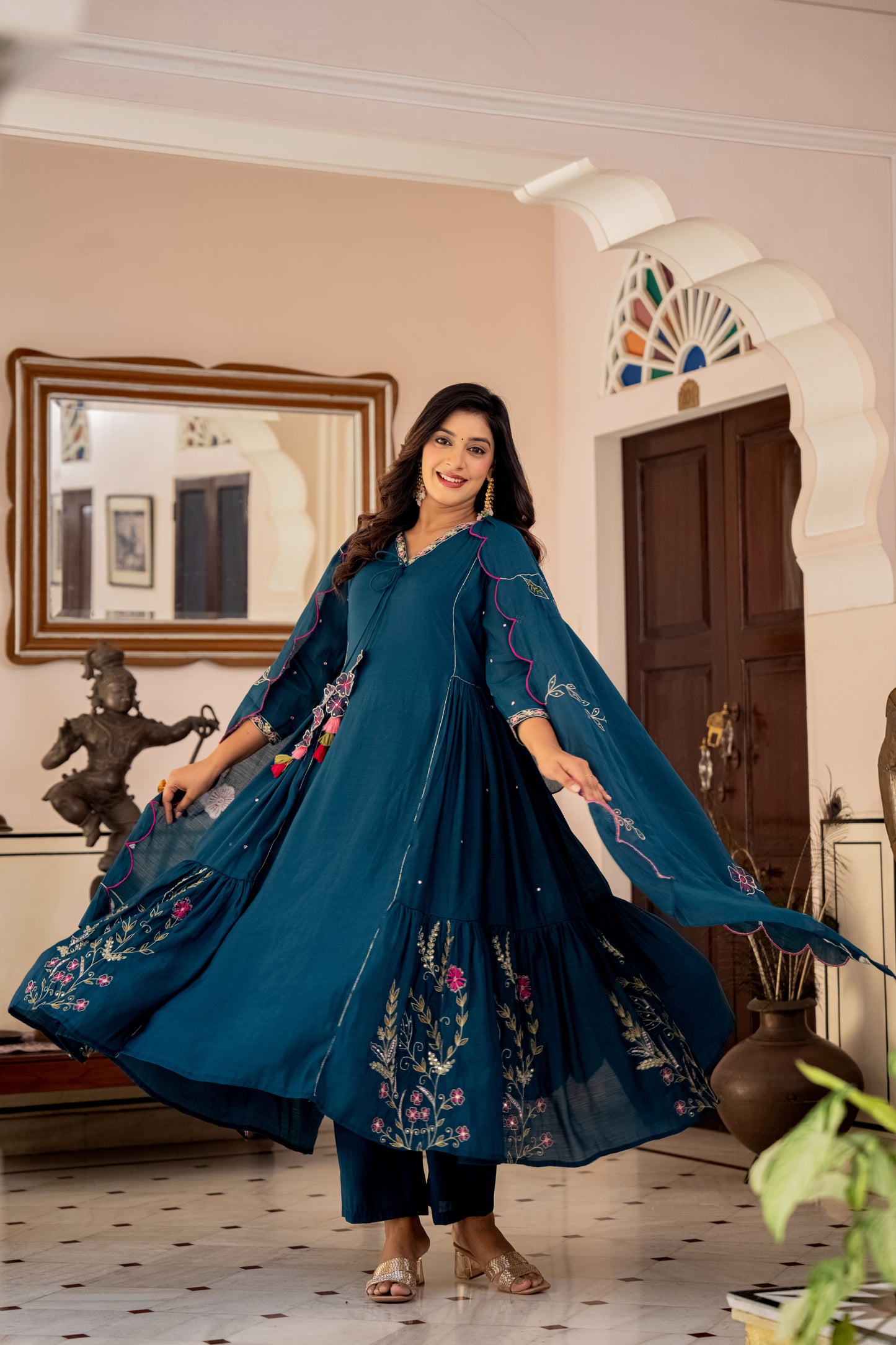 Woman in a blue embroidered kurta set standing in a decorated room.