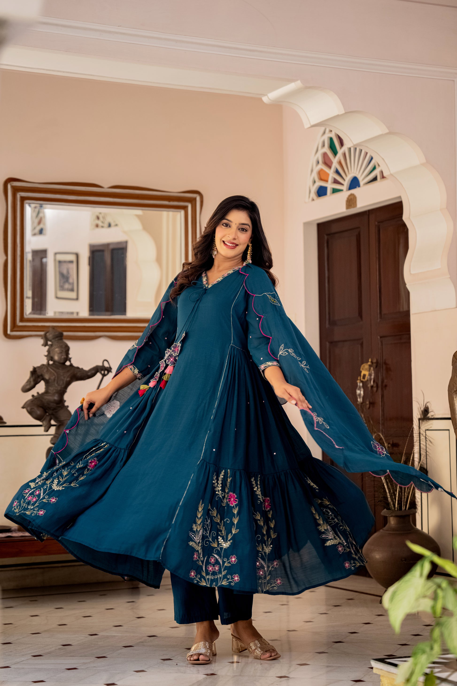 Woman in a blue embroidered kurta set standing in a decorated room.