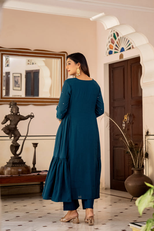 Woman in a teal dress standing in a decorated room with a statue and mirror.