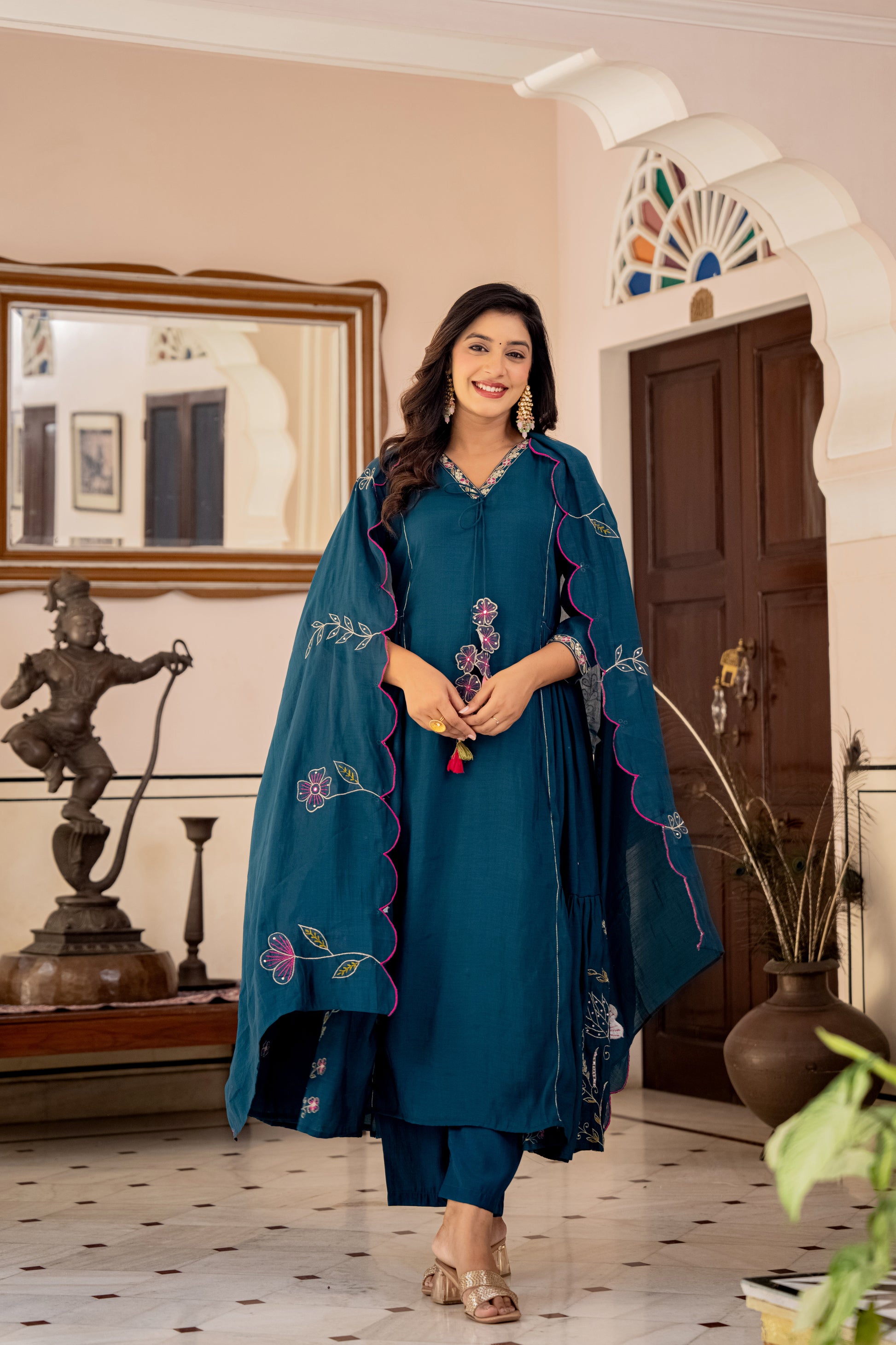 Woman in a blue embroidered outfit  which is a wedding kurta set for women standing in an indoor setting with decorative elements.