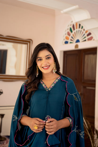 Woman in a teal traditional outfit with floral patterns indoors.