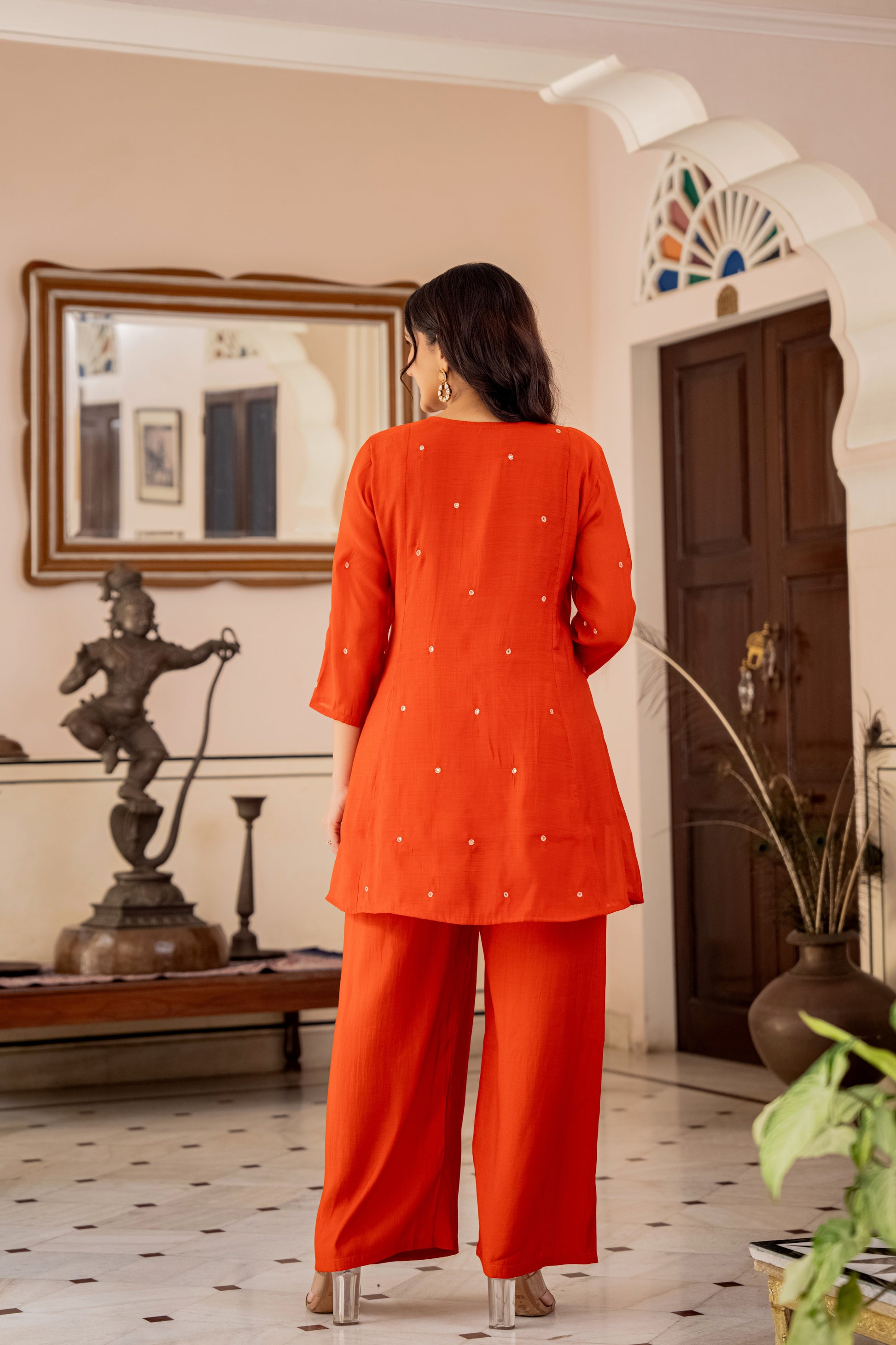 Woman in an orange outfit standing in a room with decor elements.