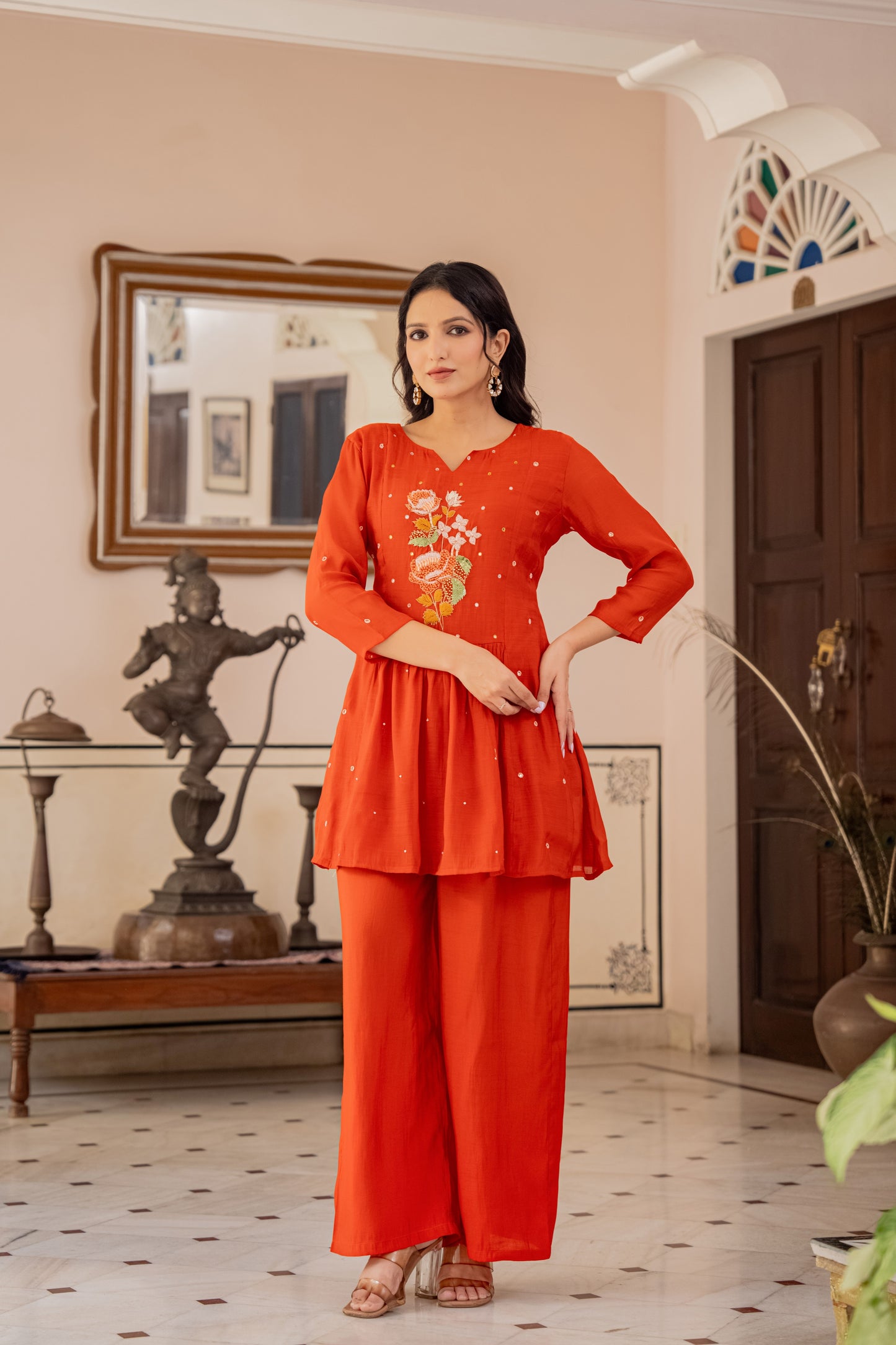 lady in an orange kurta palazzo set for women with indoor decor, resembling a traditional kurti with pant set.