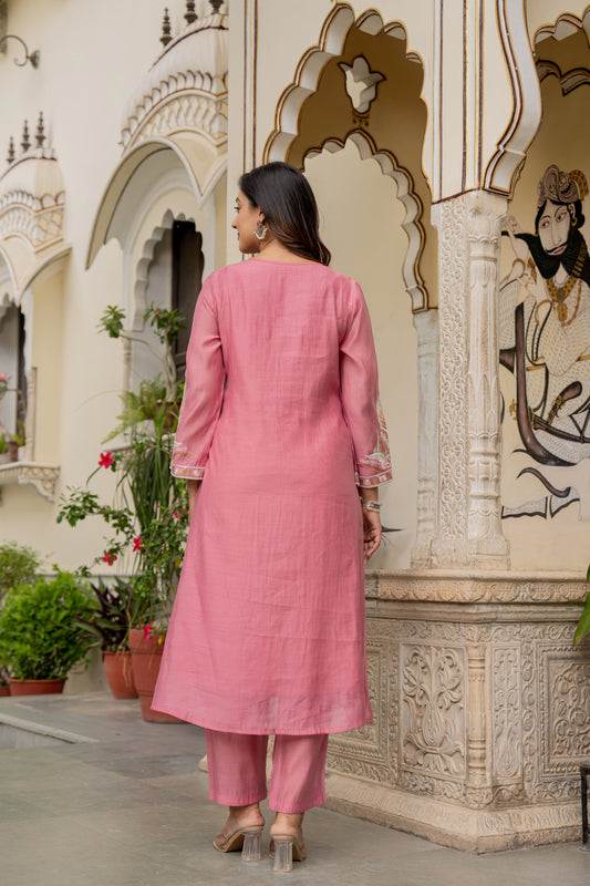 Woman in a pink traditional outfit standing in front of an ornate architectural structure.