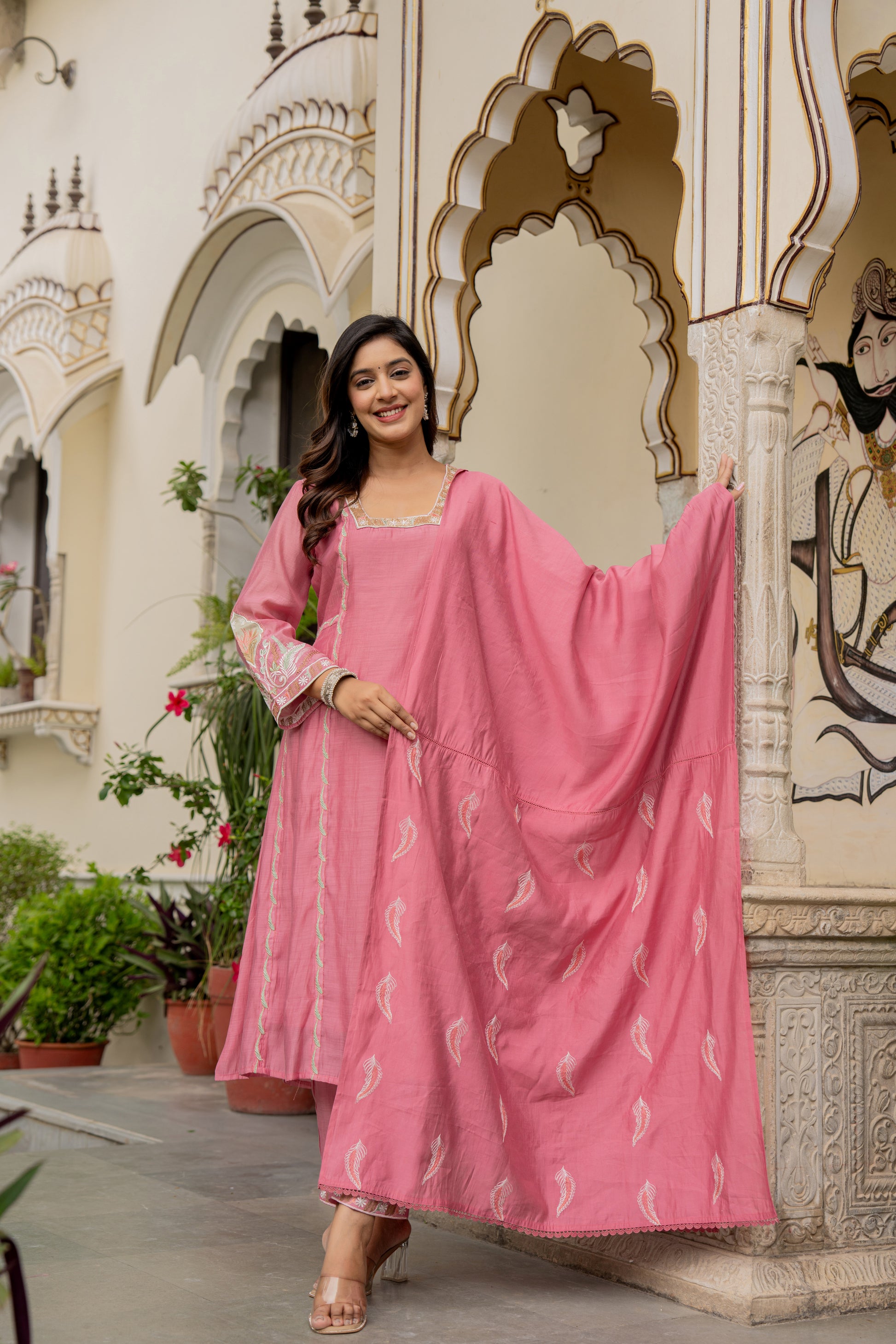 Woman in a bright pink traditional outfit standing before ornate architecture, showcasing a beautiful kurta set for wedding.