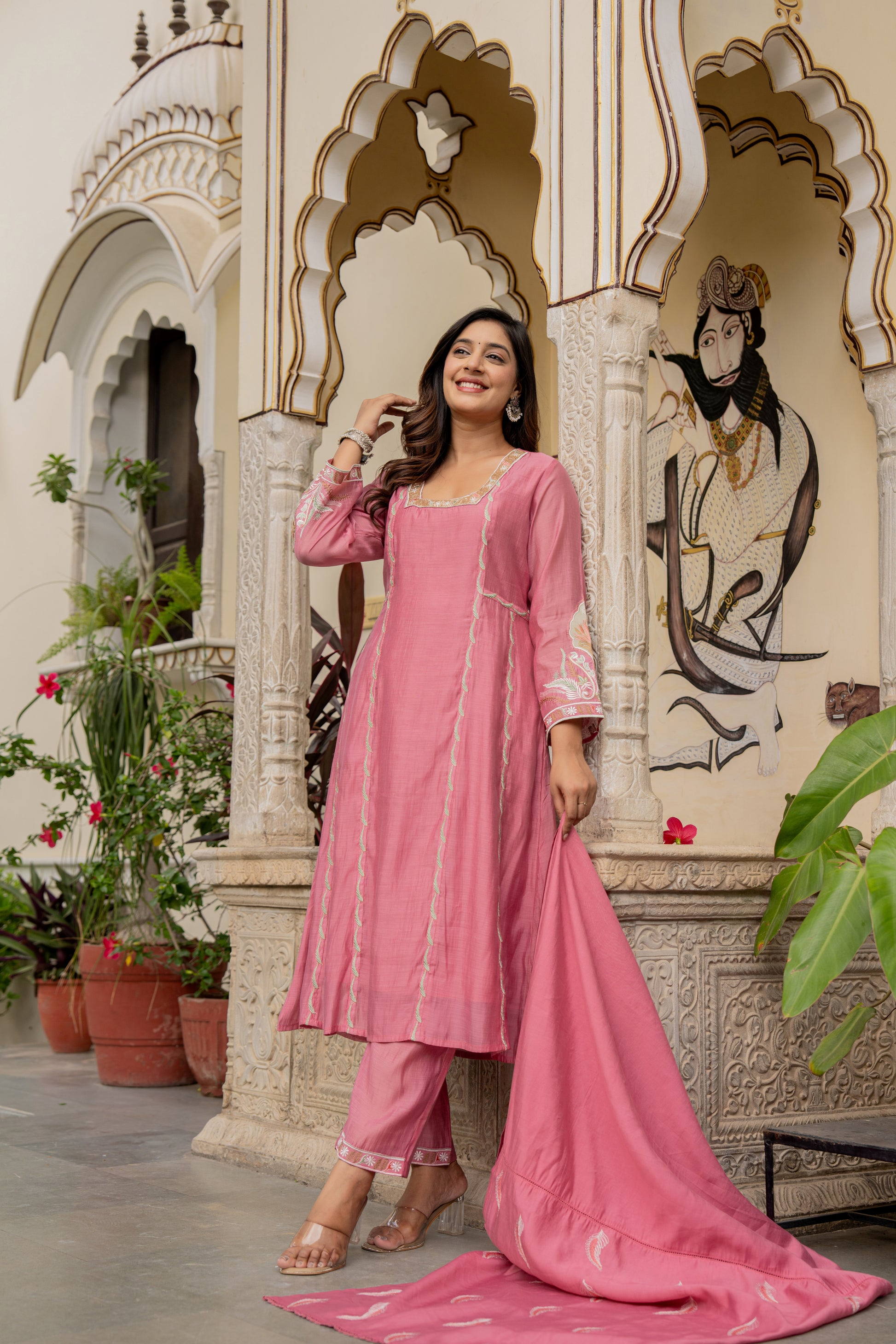 Woman in a pink traditional outfit which is wedding wear kurta set standing in front of an ornate architectural background.
