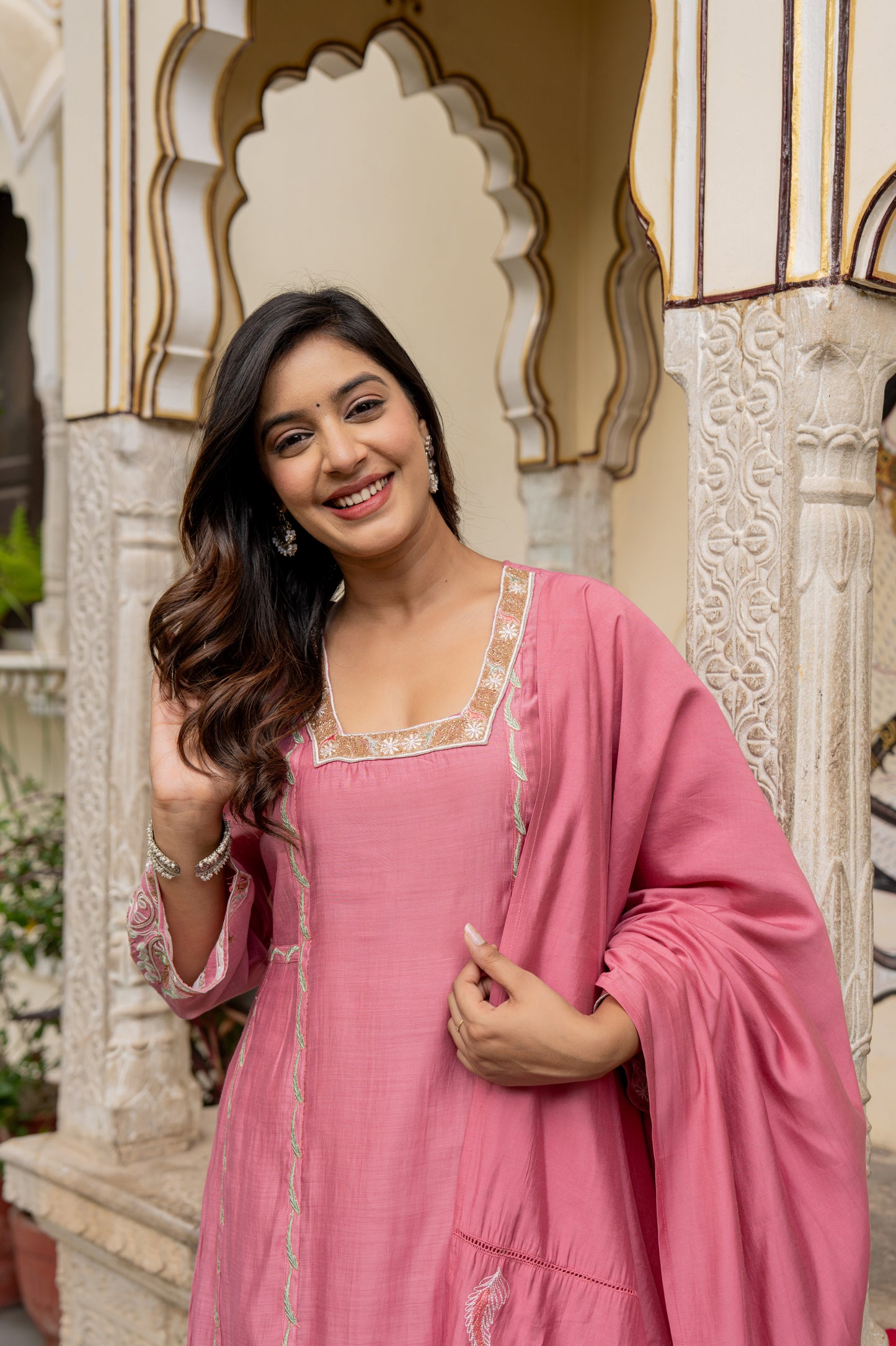 Woman in a pink traditional outfit standing in front of decorative architecture.