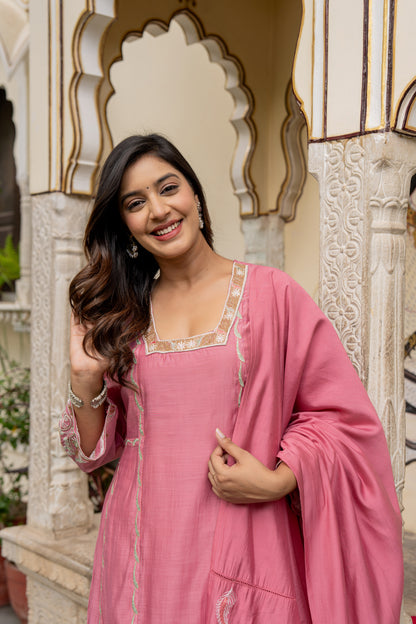 Woman in a pink traditional outfit standing in front of decorative architecture.