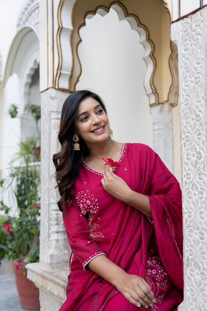 Woman in a pink traditional outfit standing in front of an ornate white archway.